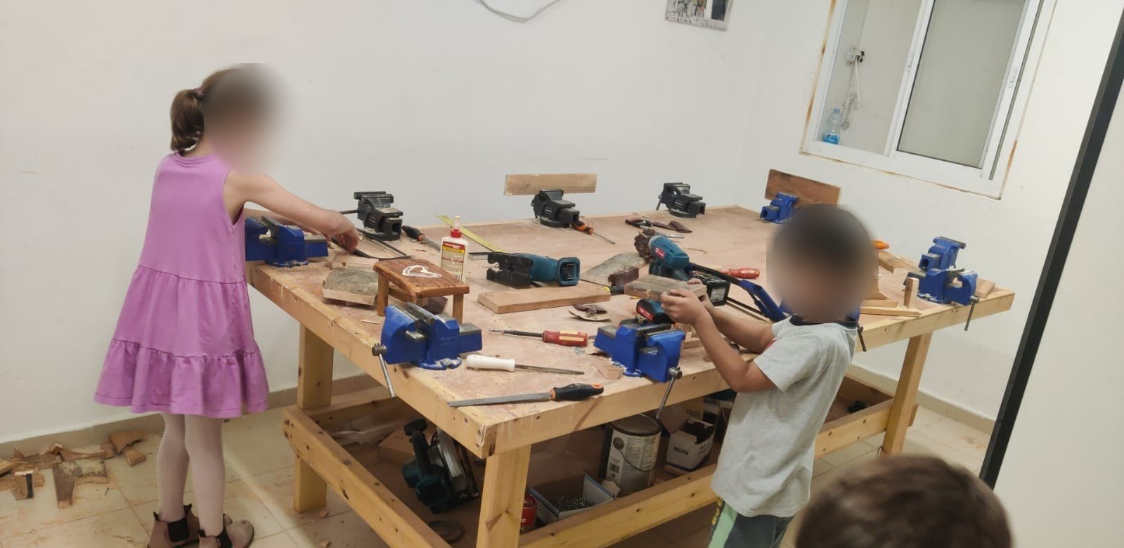 שולחן נגרות עם מלחציים וכלים, ילדים עובדים בפנים מטושטשות