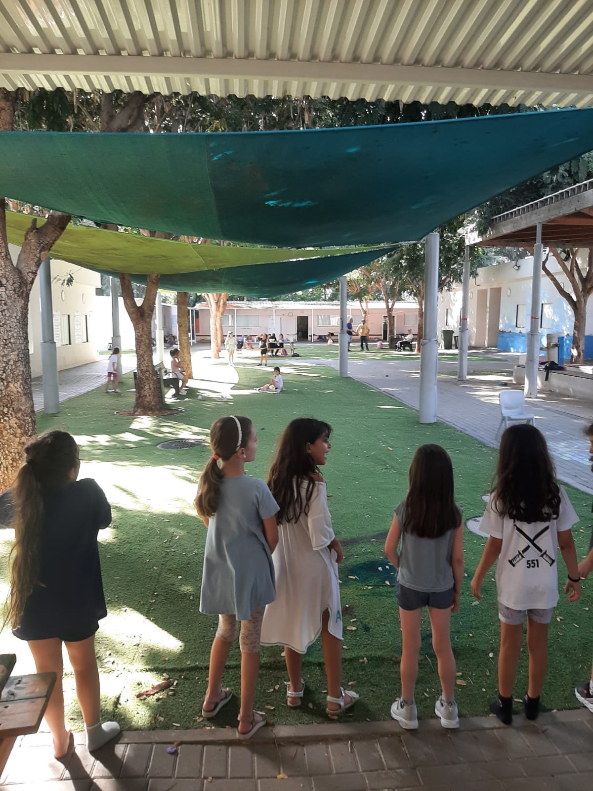 קבוצת ילדות עומדות בגבן בחצר מוצלת
